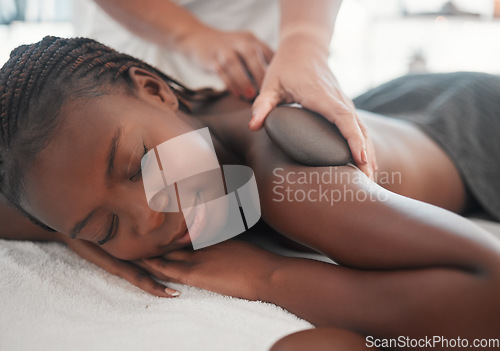 Image of Black woman gets hot stone massage, spa and hands of masseuse, holistic and wellness physical therapy. Health, peace with face and self care with zen, stress relief for people and back skin detox