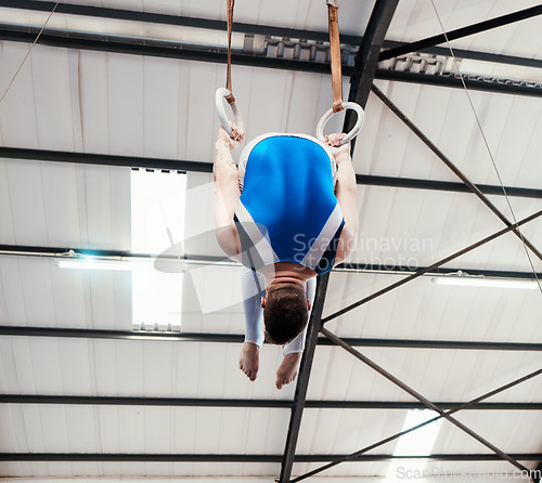 Image of Man, acrobat and gymnast turning on rings in fitness for practice, training or workout at gym. Professional male gymnastics hanging on ring circles for athletics, balance or strength exercise indoors