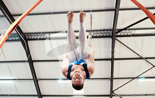 Image of Man, acrobat and gymnastics upside down on rings in fitness for practice, training or workout at gym. Professional male gymnast hanging on ring circles for athletics, acrobatics or strength exercise