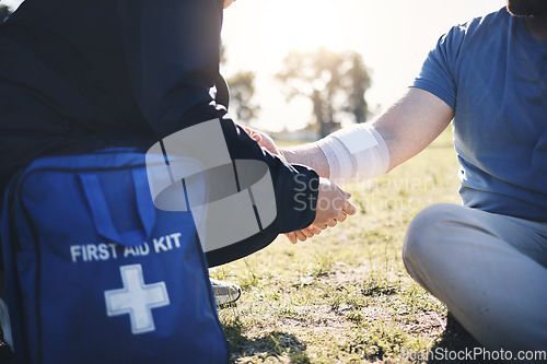 Image of First aid, help and arm injury by man with medic on the ground during morning cardio outdoors. Medical, emergency service and injured male with bandage on a field after exercise, workout or walk