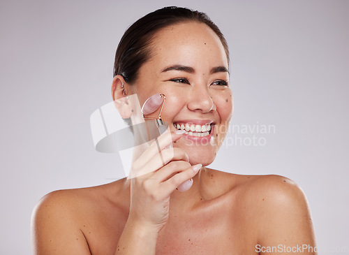 Image of Face skincare, beauty and Asian woman with jade roller in studio isolated on gray background. Dermatology aesthetics, thinking or happy female model with rose quartz stone or crystal for skin health.