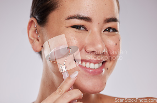 Image of Face skincare, portrait and Asian woman with roller in studio isolated on gray background. Dermatology aesthetics, beauty and happy female model with rose quartz stone or crystal for skin health.