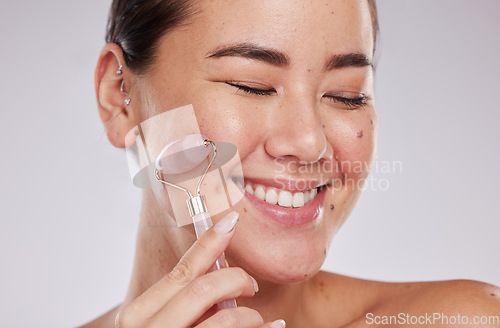 Image of Face, eyes closed and skincare of Asian woman with roller in studio isolated on a gray background. Dermatology aesthetics, beauty or happy female model with rose quartz stone or crystal for health.