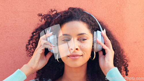 Image of Music, headphones and face of a happy black woman listening to radio, song and sound against a wall background. African female head in wireless happiness, excitement and fun audio playlist outdoors