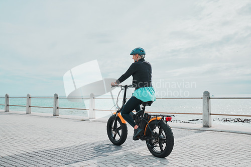 Image of Mature woman, helmet or electrical bike by beach for future fitness, clean energy transport or sustainability travel. Old person, ebike or electric bicycle with head safety for eco friendly cycling