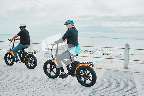 Image of Couple, helmet or electrical bike by sea or ocean beach in bonding transport, clean energy or sustainability travel. Technology, electric or eco friendly bicycle for happy woman or mature cycling man