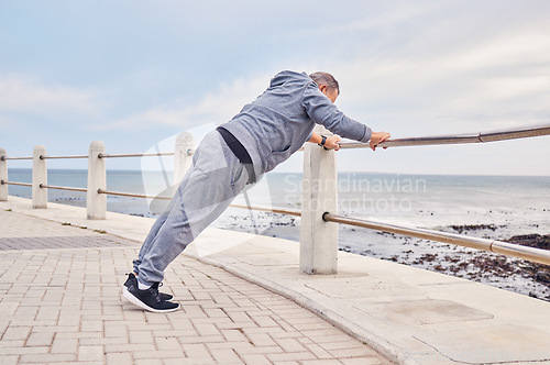 Image of Senior man, fitness and stretching at beach sidewalk for energy, wellness and healthy cardio workout. Elderly male, warm up and exercise at seaside promenade for training, sports and body performance