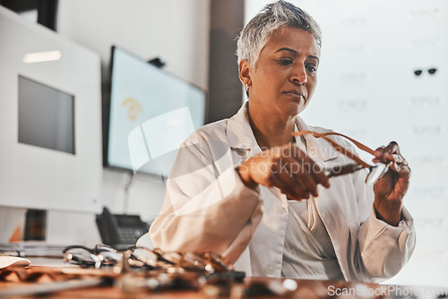 Image of Elderly optometrist woman, glasses and design for focus, vision or frame planning at desk in clinic. Senior optician, spectacle designer and eye care in workplace for fashion, small business and goal