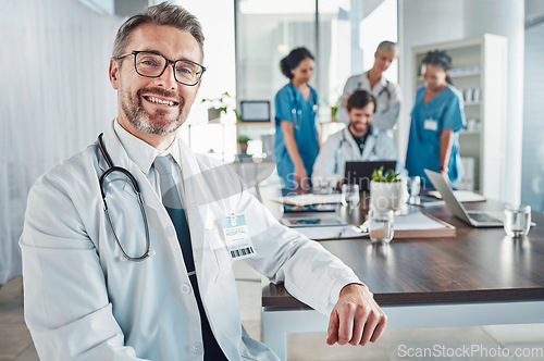 Image of Healthcare, smile and portrait of senior doctor at desk in teaching hospital office with nurses and medical students. Health, medicine and leadership with mature mentor and smiling man at clinic.