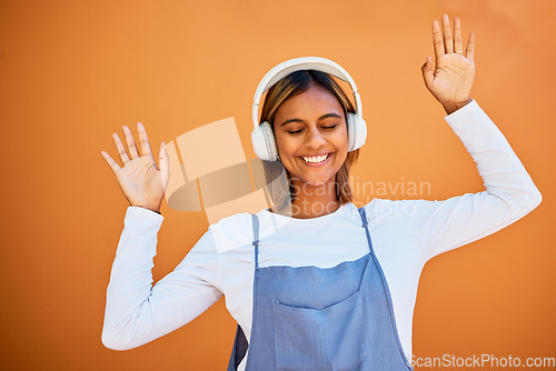 Image of Dance, happy and woman with headphones music isolated on an orange studio background. Smile, free and carefree dancing girl listening to audio, podcast or sound for entertainment and freedom