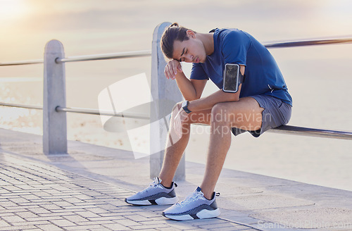 Image of Tired runner man, sitting and beach for workout, health and exercise with headache, rest and relax. Gen z guy, training burnout and challenge with breathing, mindset and fitness on railing by ocean