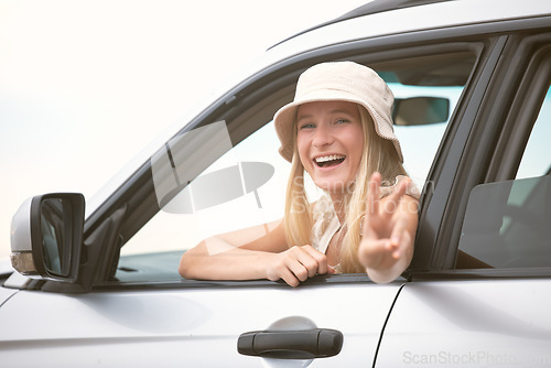 Image of One beautiful blonde caucasian woman gesturing peace while enjoying a roadtrip. An attractive young female leaning out of the passenger window of a car while taking a drive. Enjoying the open road