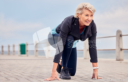 Image of Senior woman, starting position and running outdoor at beach promenade, exercise or sky mockup. Elderly lady ready to run for fitness, cardio training and smile for sports marathon, health or mindset
