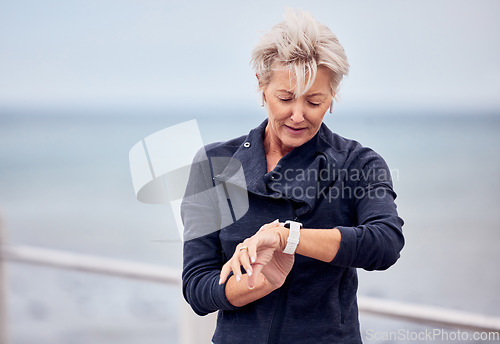 Image of Smart watch, senior woman and fitness outdoor at beach promenade, exercise or sky mockup. Stopwatch, sports lady and runner check time, heart rate and monitor healthy body progress, clock or data app