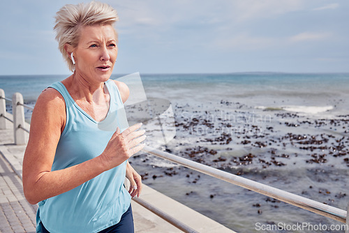 Image of Senior woman, exercise and running at beach promenade, sky mockup or energy of health, wellness and workout. Elderly female, earphones and fitness at ocean of sports, cardio runner and strong mindset