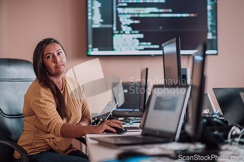 Image of A businesswoman sitting in a programmer's office surrounded by computers, showing her expertise and dedication to technology.