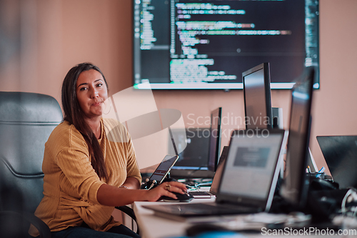 Image of A businesswoman sitting in a programmer's office surrounded by computers, showing her expertise and dedication to technology.