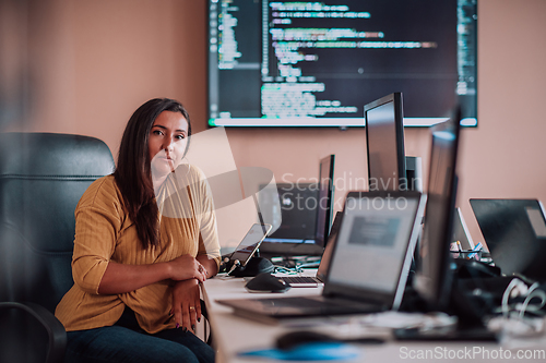 Image of A businesswoman sitting in a programmer's office surrounded by computers, showing her expertise and dedication to technology.