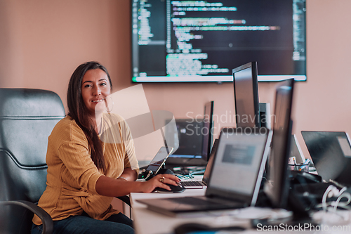 Image of A businesswoman sitting in a programmer's office surrounded by computers, showing her expertise and dedication to technology.