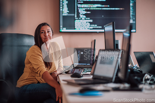 Image of A businesswoman sitting in a programmer's office surrounded by computers, showing her expertise and dedication to technology.