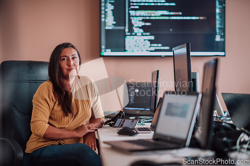 Image of A businesswoman sitting in a programmer's office surrounded by computers, showing her expertise and dedication to technology.