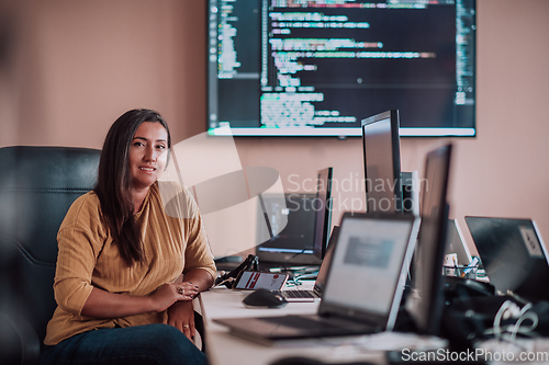 Image of A businesswoman sitting in a programmer's office surrounded by computers, showing her expertise and dedication to technology.