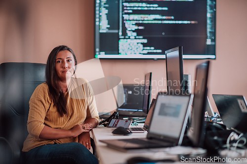 Image of A businesswoman sitting in a programmer's office surrounded by computers, showing her expertise and dedication to technology.