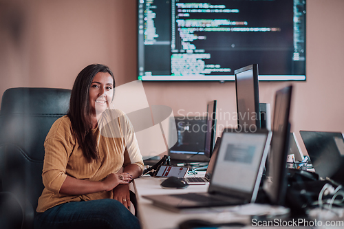 Image of A businesswoman sitting in a programmer's office surrounded by computers, showing her expertise and dedication to technology.