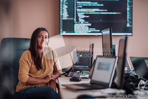 Image of A businesswoman sitting in a programmer's office surrounded by computers, showing her expertise and dedication to technology.