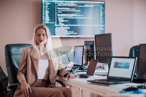 Image of A businesswoman sitting in a programmer's office surrounded by computers, showing her expertise and dedication to technology.