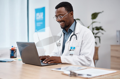 Image of Black man, doctor and laptop with smile in healthcare for research, medicine or PHD at clinic desk. Happy African American male medical professional smiling, working or typing on computer at hospital