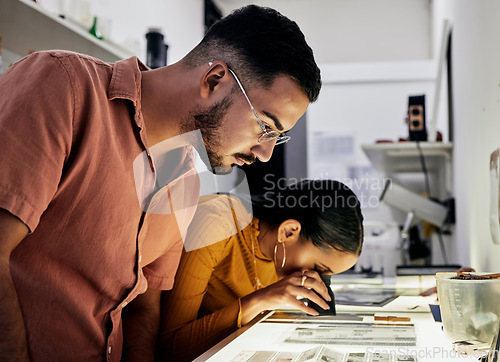 Image of Photographer, editing and film negatives with looking, magnifying glass for zoom analysis at photo journalist job. Photography man, analyse or focus with woman in studio for creative decision in team