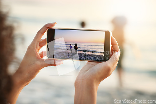 Image of Phone, photograph and beach with a woman in nature, recording her playing kids by the ocean outdoor. Mobile, family and sunset with a parent taking a picture of her kids on the sand at the sea