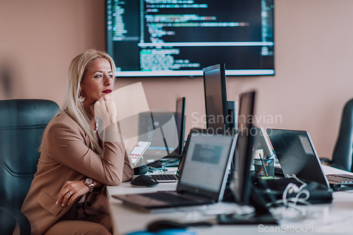 Image of A businesswoman sitting in a programmer's office surrounded by computers, showing her expertise and dedication to technology.