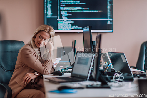 Image of A businesswoman sitting in a programmer's office surrounded by computers, showing her expertise and dedication to technology.