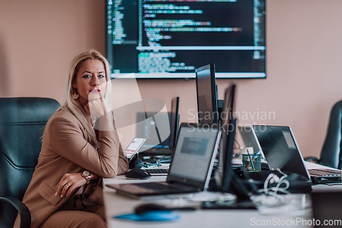 Image of A businesswoman sitting in a programmer's office surrounded by computers, showing her expertise and dedication to technology.