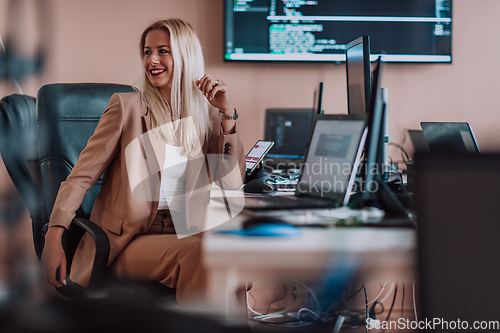 Image of A businesswoman sitting in a programmer's office surrounded by computers, showing her expertise and dedication to technology.