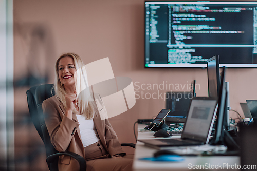 Image of A businesswoman sitting in a programmer's office surrounded by computers, showing her expertise and dedication to technology.