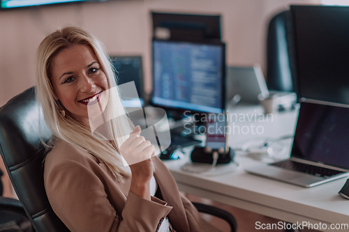 Image of A businesswoman sitting in a programmer's office surrounded by computers, showing her expertise and dedication to technology.