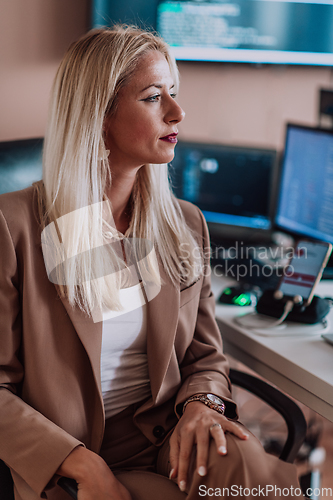 Image of A businesswoman sitting in a programmer's office surrounded by computers, showing her expertise and dedication to technology.