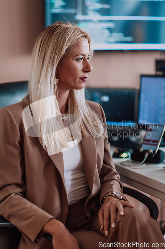 Image of A businesswoman sitting in a programmer's office surrounded by computers, showing her expertise and dedication to technology.