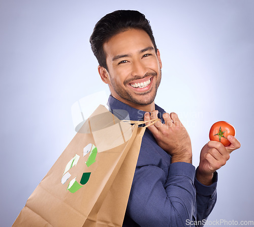 Image of Man in portrait, happy and recycling paper bag with tomato and sustainable shopping on studio background. Eco friendly, vegetable and climate change awareness in retail, sustainability and health