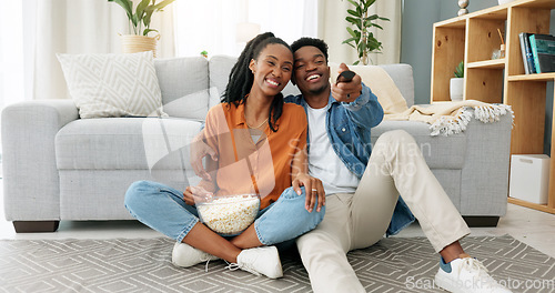 Image of Happy black couple, eating popcorn and a movie playing in the living room of their home or house. Love, romance and man and woman having leisure time while looking at tv and browsing channels.