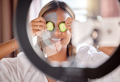 Image of Woman, vlogger and ring light of skincare influencer holding cucumber on eyes for facial wellness at home. Happy female with beauty face mask smiling for online vlog, social media post or streaming