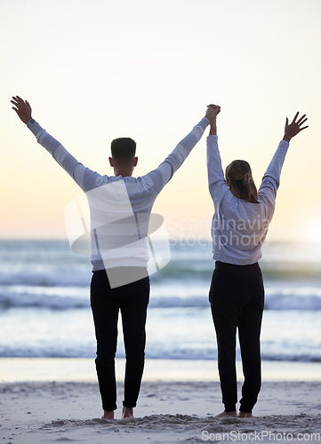 Image of Couple, beach and hands up outdoor while happy at sunset for love, freedom and peace with calm ocean. Young man and woman together on vacation holiday at sea to relax, travel and connect in nature