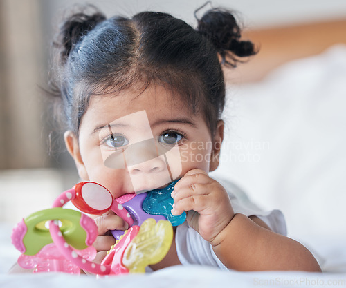 Image of Portrait, baby girl and biting toys in bedroom, house and home for development, growth and teething progress. Cute kid, face and chewing rattle in mouth for tooth, child and playing in nursery room