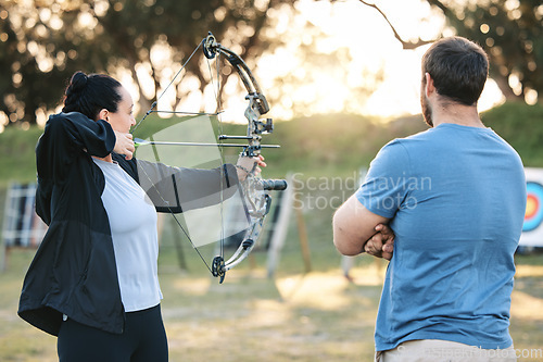 Image of Archery, sports or help with a woman holding a bow and arrow outdoor for target practice with a coach. Coaching, learning or advice with a female and trainer at the shooting range for weapon training