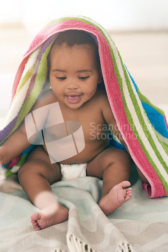 Image of African baby, girl and sitting for smile with blanket, young or healthy in bedroom at family home. Black infant, toddler and bed with towel for growth, care and health in morning sunshine at house