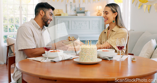 Image of Interracial, couple and celebrate for birthday with gift, being happy and relax together at party. Romance, man and woman with present, bonding and smile in home in living room for hug or celebration