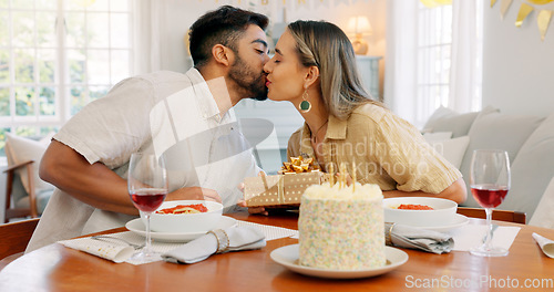 Image of Interracial couple, gift and celebrate birthday being happy, kiss and smile in home at table with cake. Love, man and woman being content, romantic and present being cheerful celebration together.